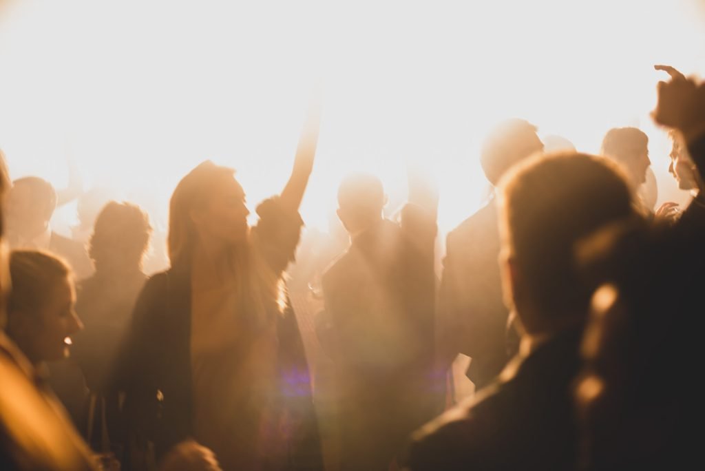Cinematic silhouettes of wedding guests partying under warm golden lights. Creative documentary wedding photography.