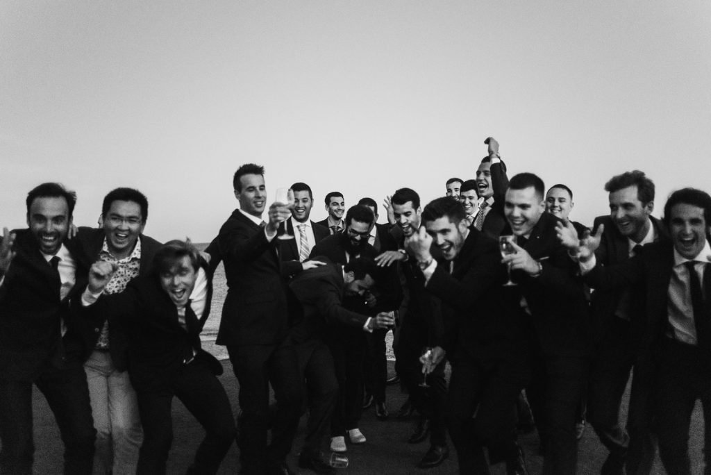 Black and white documentary photo of groom and friends celebrating spontaneously. Candid wedding photographer.