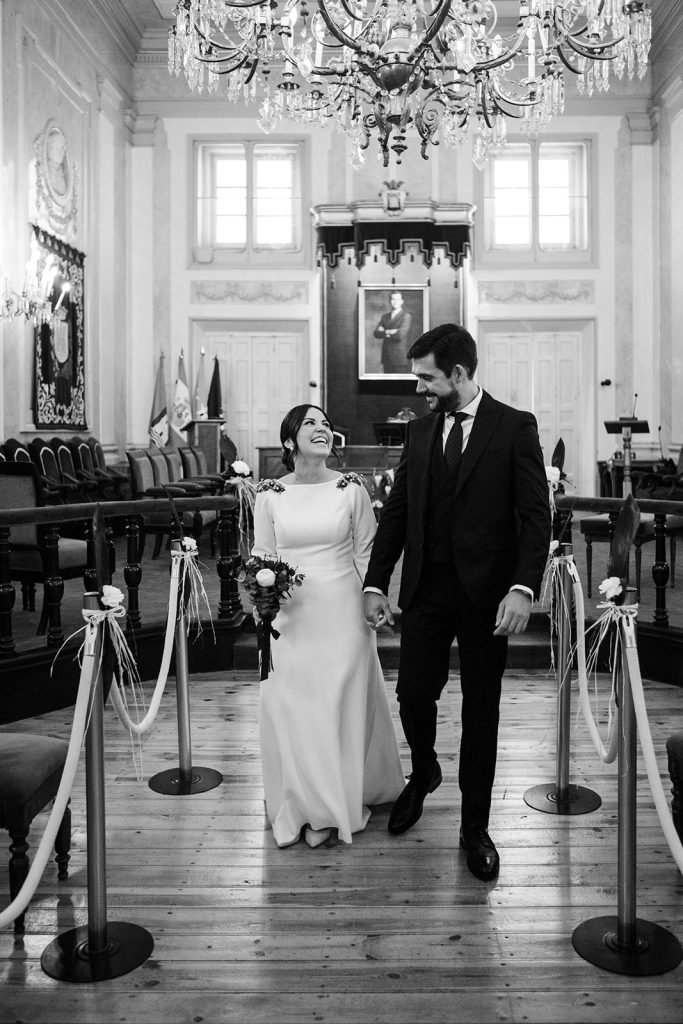 Documentary black and white photograph of a bride and groom holding hands inside a historic church during their wedding ceremony in Madrid. Authentic wedding photography by Flor de Sal Photo.
