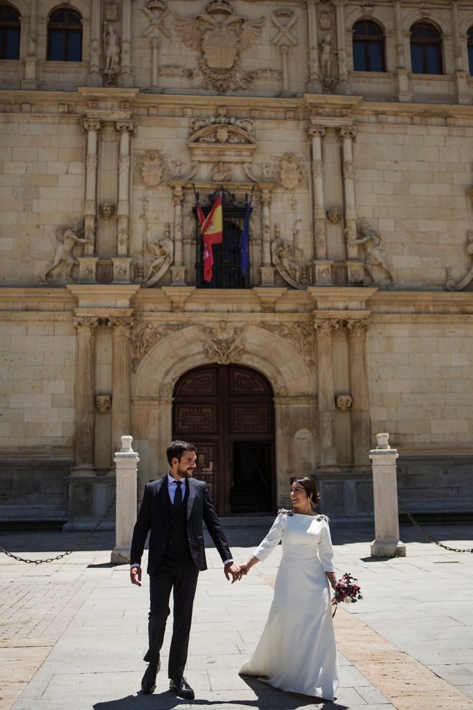 Bride and groom walking hand in hand in front of a stunning historic church facade in Madrid. Destination wedding photography Madrid by Flor de Sal Photo.