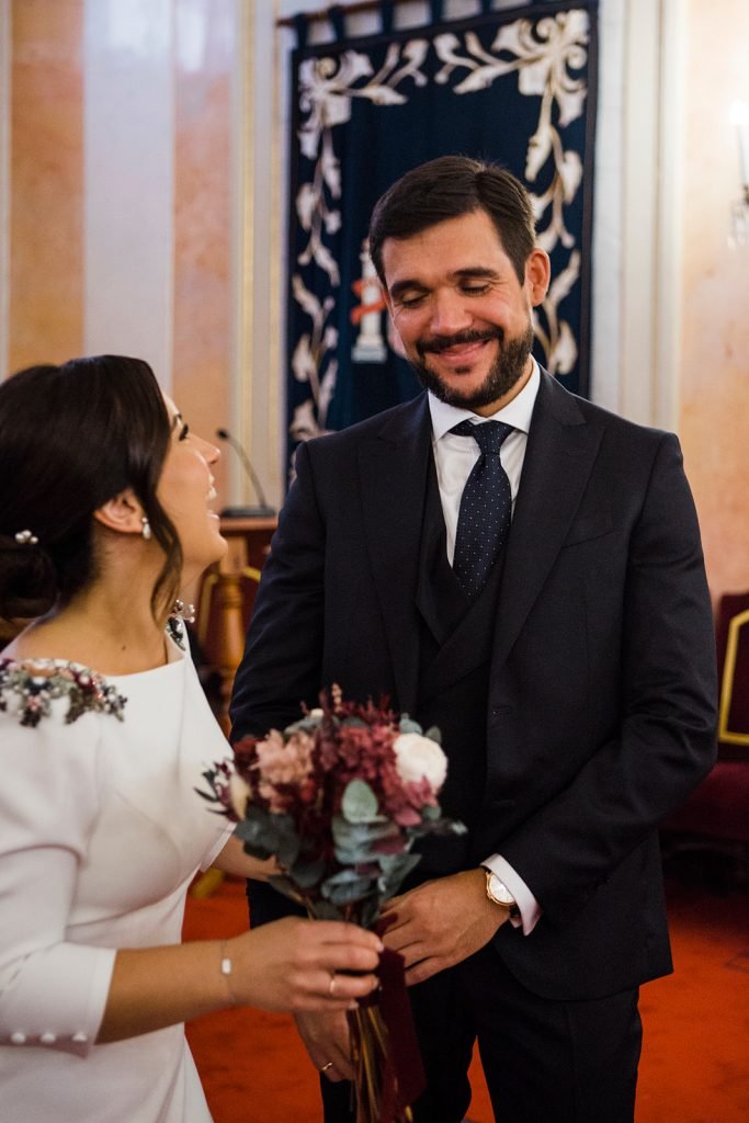 Candid wedding couple laughing and holding the bridal bouquet inside a traditional Spanish church during their ceremony service. Natural wedding photographer Madrid Flor de Sal Photo